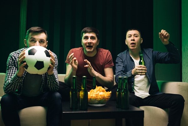 Three happy caucasian friendly men eating chips snacks and cheering up for football game